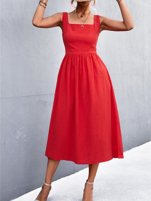 A woman in a Women's Sleeve Less Dress, featuring a vibrant red hue and crafted from 100% polyester, stands against a gray wall. She accessorizes with a wide-brimmed hat, holds a straw handbag, and complements her outfit with beige sandals.