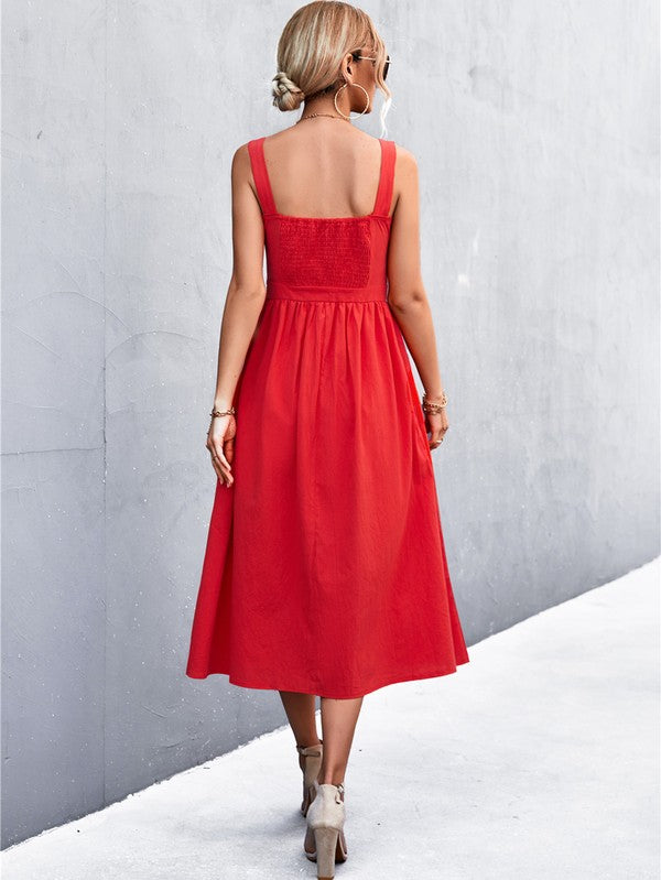 A woman in a Women's Sleeve Less Dress, featuring a vibrant red hue and crafted from 100% polyester, stands against a gray wall. She accessorizes with a wide-brimmed hat, holds a straw handbag, and complements her outfit with beige sandals.