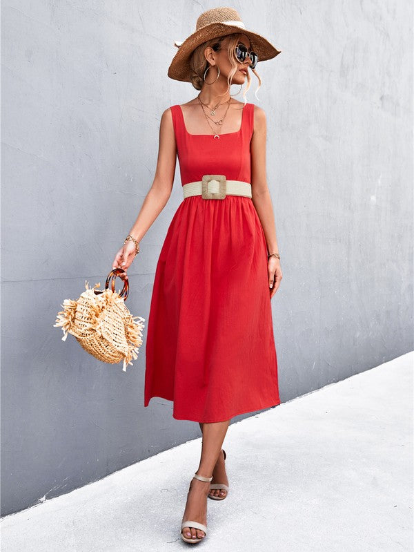 A woman in a Women's Sleeve Less Dress, featuring a vibrant red hue and crafted from 100% polyester, stands against a gray wall. She accessorizes with a wide-brimmed hat, holds a straw handbag, and complements her outfit with beige sandals.