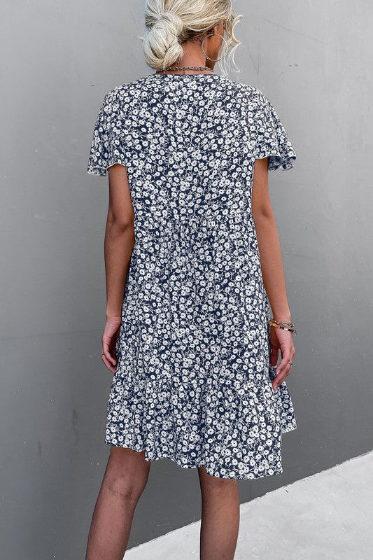 Individual wearing a Floral Short Sleeve V Neck Midi Length Dress stands against a gray wall.