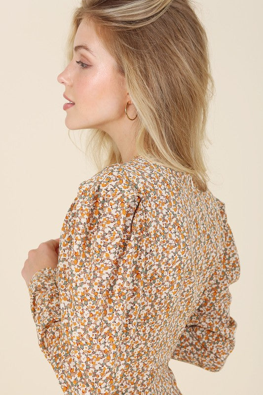 A woman gracefully poses against a beige background wearing the Fit and Flare floral maxi dress, featuring a V-neckline, elegant puff sleeves, and a complementary front slit.