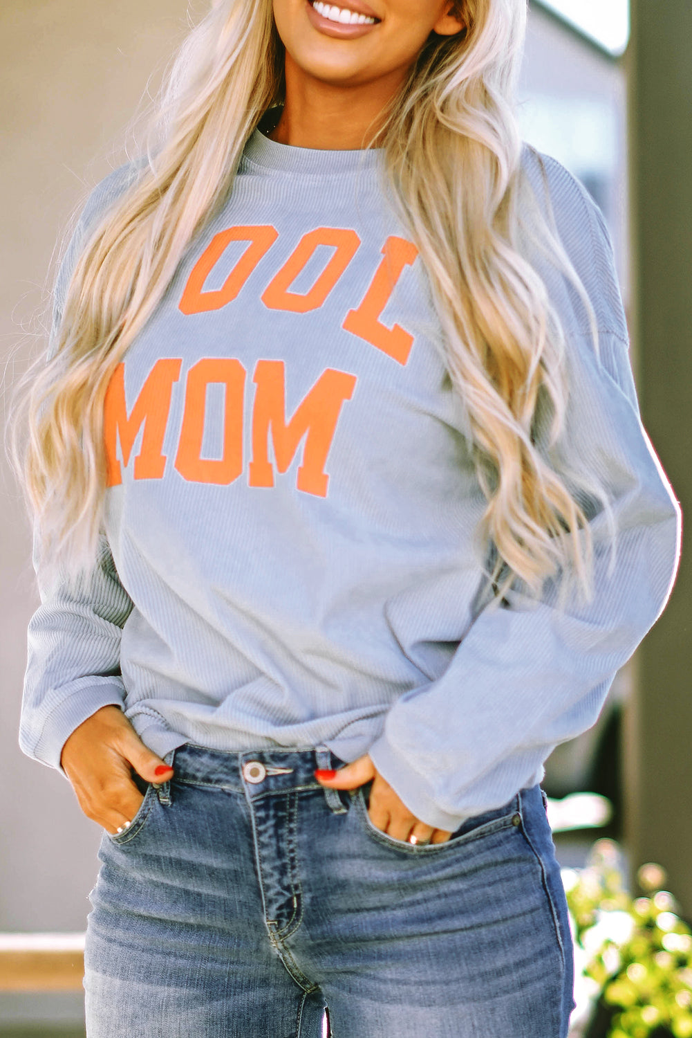 A person with long blonde hair stands facing away, wearing a Gray Cool Mom Graphic Print Cording Sweatshirt and blue jeans.