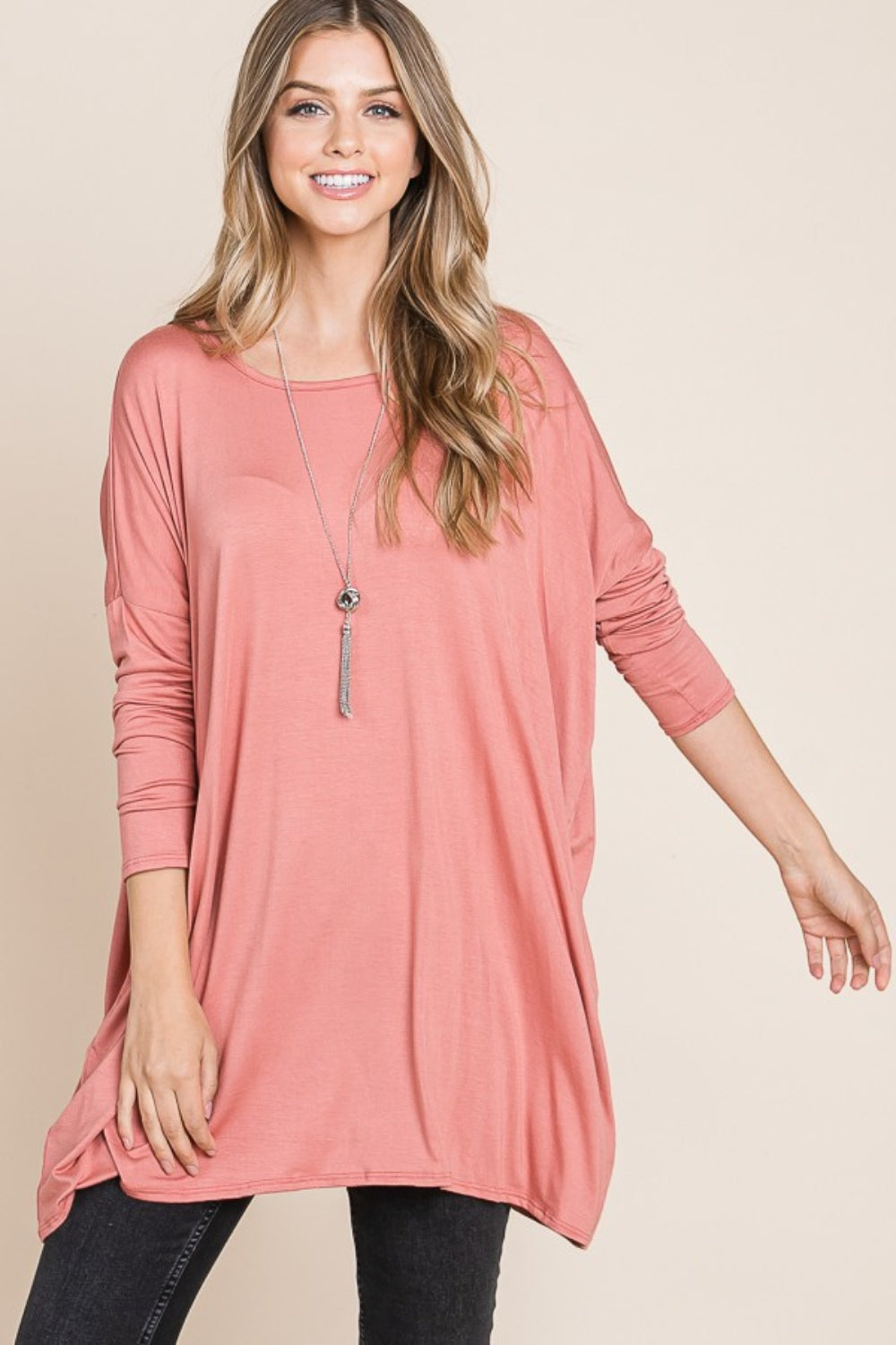 Person in a pink BOMBOM Round Neck Long Sleeve Oversized Top, wearing a long necklace, standing against a neutral background, and posing with one hand touching their hair. This oversized top is made from comfortable fabric that adds to the relaxed vibe.