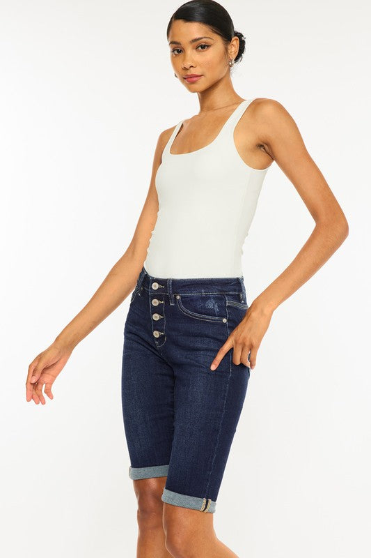 A woman wearing a white tank top and High Rise Button Down Cuffed Bermuda Jeans.