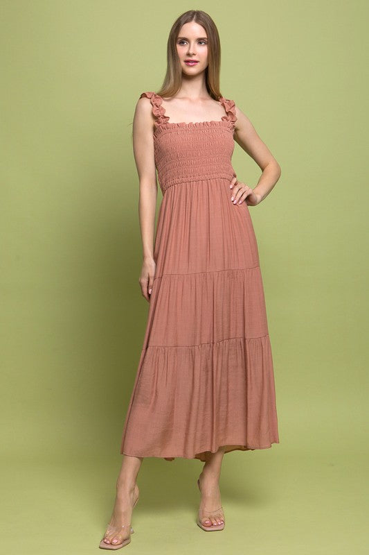 A person models the Smocked Bodice Maxi Dress, featuring a bright green hue, ruffled straps, and a sleeveless design, standing elegantly against a plain background.