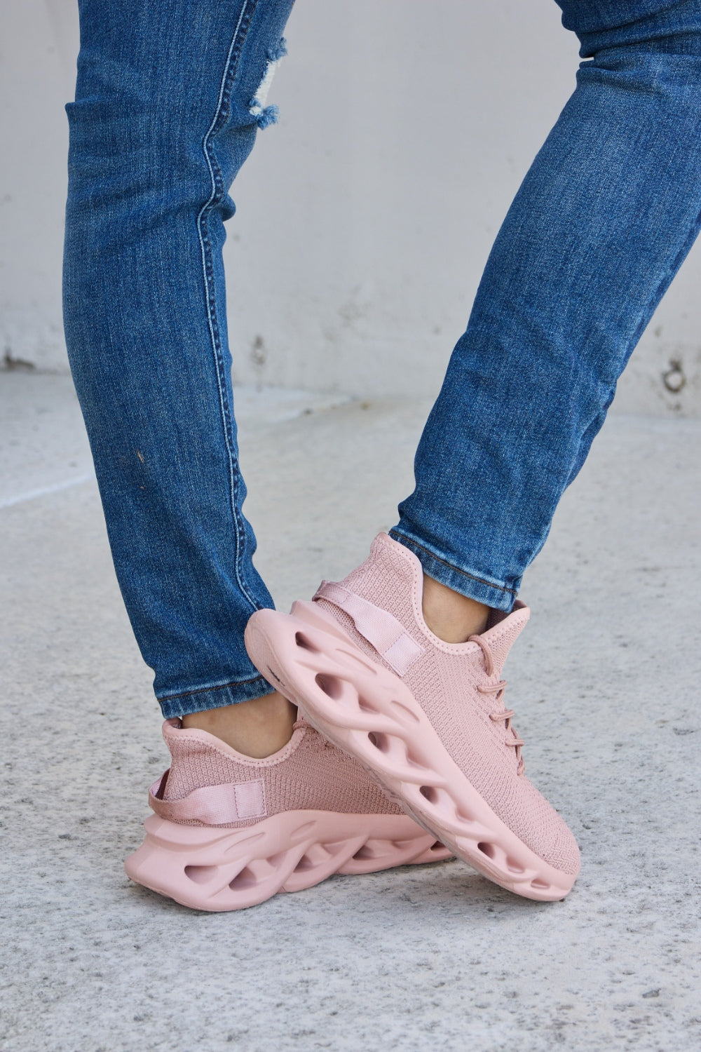 Person wearing blue ripped jeans and Forever Link Mesh Breathable Platform Athletic Shoes in light pink, standing on a concrete surface.