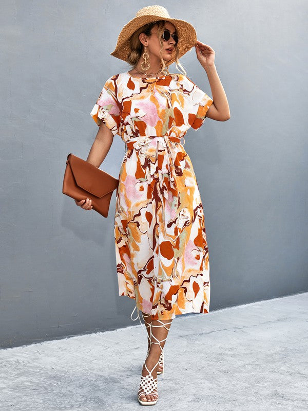 A woman in a Women Print Round Neck Short Sleeve Dress, complemented by a straw hat and sunglasses, gracefully strolls across a gray textured surface.