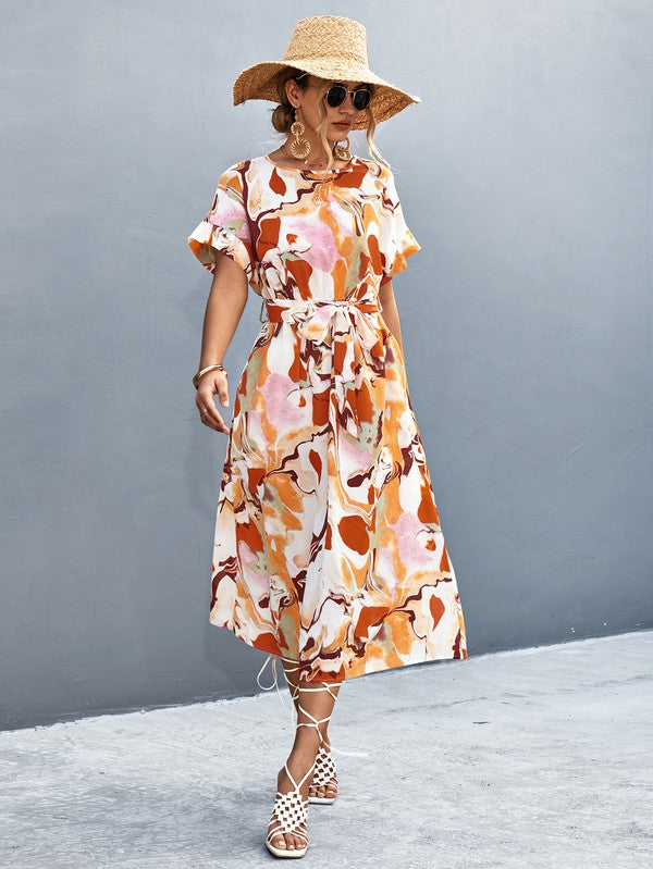 A woman in a Women Print Round Neck Short Sleeve Dress, complemented by a straw hat and sunglasses, gracefully strolls across a gray textured surface.