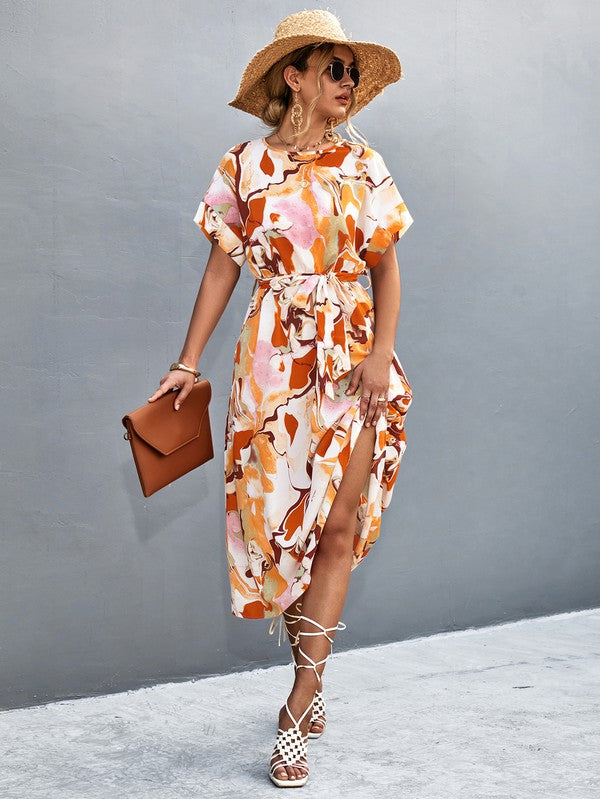 A woman in a Women Print Round Neck Short Sleeve Dress, complemented by a straw hat and sunglasses, gracefully strolls across a gray textured surface.