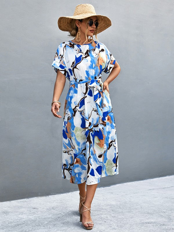 A woman in a Women Print Round Neck Short Sleeve Dress, complemented by a straw hat and sunglasses, gracefully strolls across a gray textured surface.