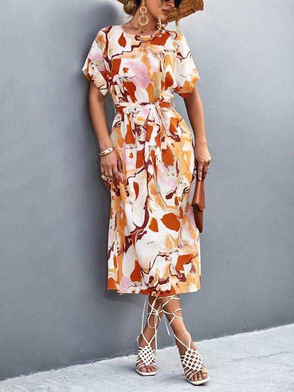 A woman in a Women Print Round Neck Short Sleeve Dress, complemented by a straw hat and sunglasses, gracefully strolls across a gray textured surface.