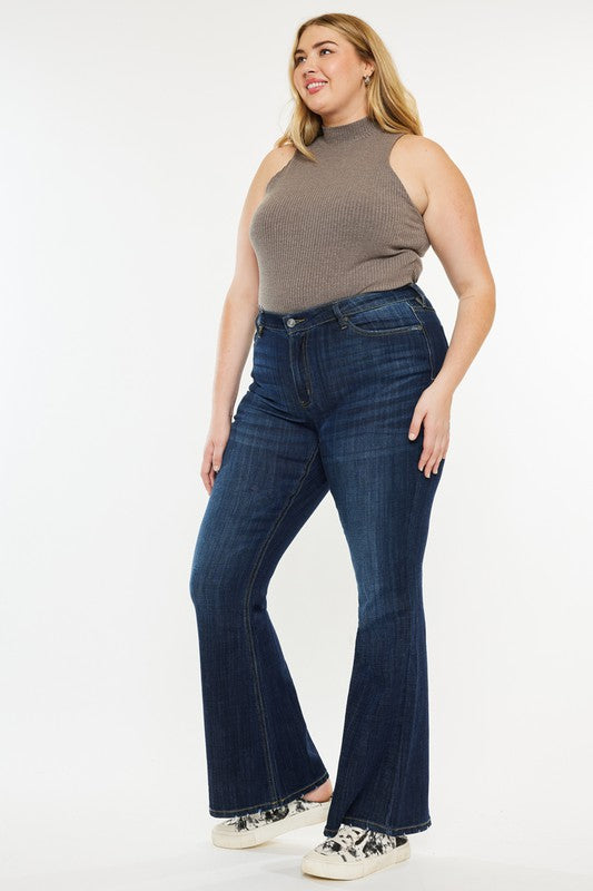 A person wearing a sleeveless gray top, Plus Petite Dark Wash Mid Rise Flare Jeans, and white sneakers. The image is labeled "Plus Petite.