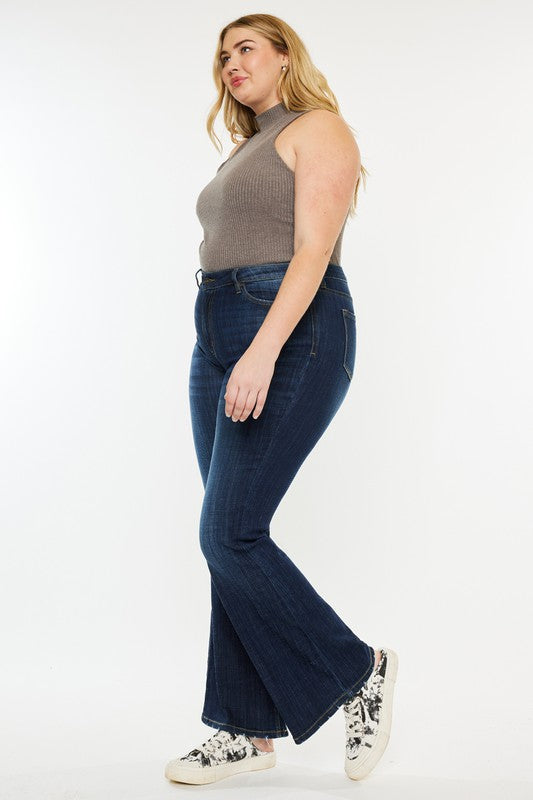 A person wearing a sleeveless gray top, Plus Petite Dark Wash Mid Rise Flare Jeans, and white sneakers. The image is labeled "Plus Petite.