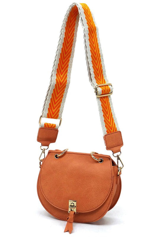 The Fashion Flap Saddle Satchel Crossbody Bag is a light pink handbag crafted from faux vegan leather and adorned with gold hardware. It features a buckle clasp and comes with a detachable, wide strap that has a red and black chevron pattern with pink trim, allowing it to double as a chic crossbody bag.