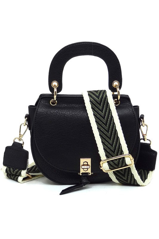 The Fashion Flap Saddle Satchel Crossbody Bag is a light pink handbag crafted from faux vegan leather and adorned with gold hardware. It features a buckle clasp and comes with a detachable, wide strap that has a red and black chevron pattern with pink trim, allowing it to double as a chic crossbody bag.