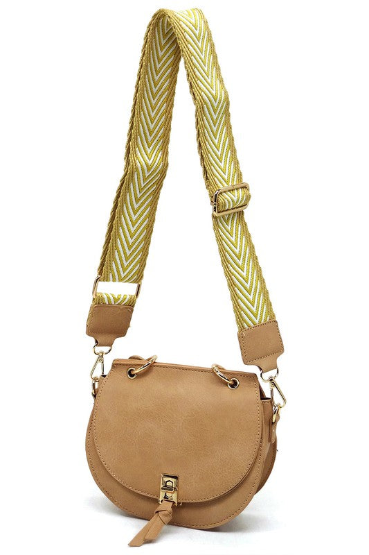 The Fashion Flap Saddle Satchel Crossbody Bag is a light pink handbag crafted from faux vegan leather and adorned with gold hardware. It features a buckle clasp and comes with a detachable, wide strap that has a red and black chevron pattern with pink trim, allowing it to double as a chic crossbody bag.