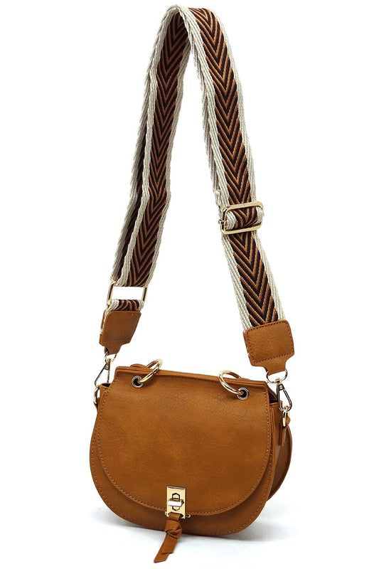 The Fashion Flap Saddle Satchel Crossbody Bag is a light pink handbag crafted from faux vegan leather and adorned with gold hardware. It features a buckle clasp and comes with a detachable, wide strap that has a red and black chevron pattern with pink trim, allowing it to double as a chic crossbody bag.