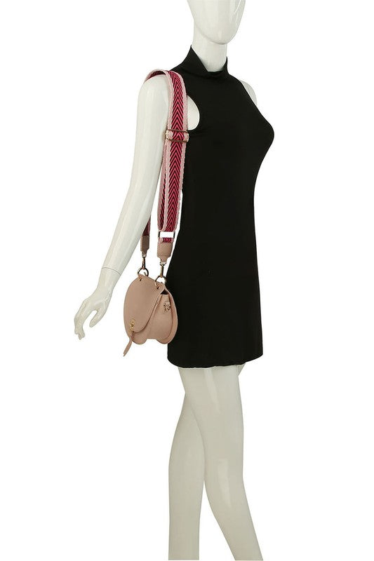 The Fashion Flap Saddle Satchel Crossbody Bag is a light pink handbag crafted from faux vegan leather and adorned with gold hardware. It features a buckle clasp and comes with a detachable, wide strap that has a red and black chevron pattern with pink trim, allowing it to double as a chic crossbody bag.