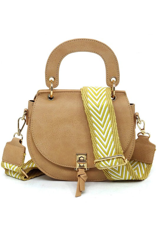 The Fashion Flap Saddle Satchel Crossbody Bag is a light pink handbag crafted from faux vegan leather and adorned with gold hardware. It features a buckle clasp and comes with a detachable, wide strap that has a red and black chevron pattern with pink trim, allowing it to double as a chic crossbody bag.