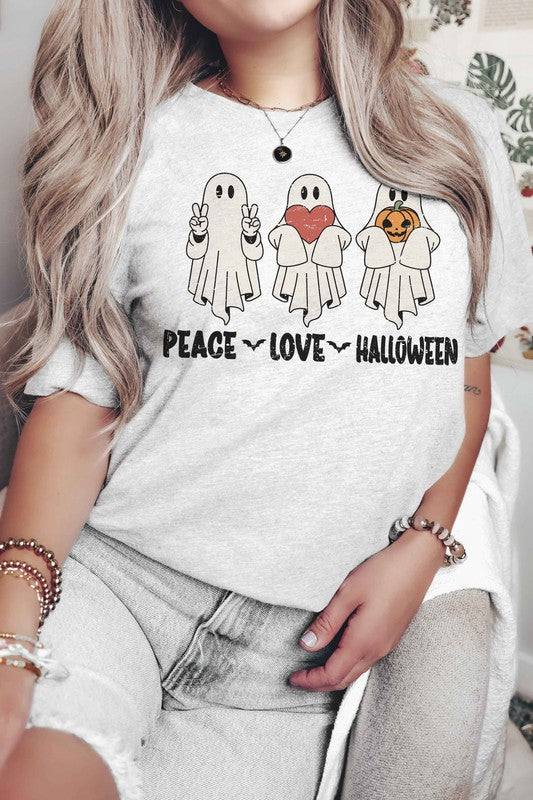 A person wearing the PEACE LOVE HALLOWEEN Graphic Tee, which features three cartoon ghosts—one making a peace sign, another holding a heart, and the third with a pumpkin—along with the words "PEACE LOVE HALLOWEEN" printed underneath.