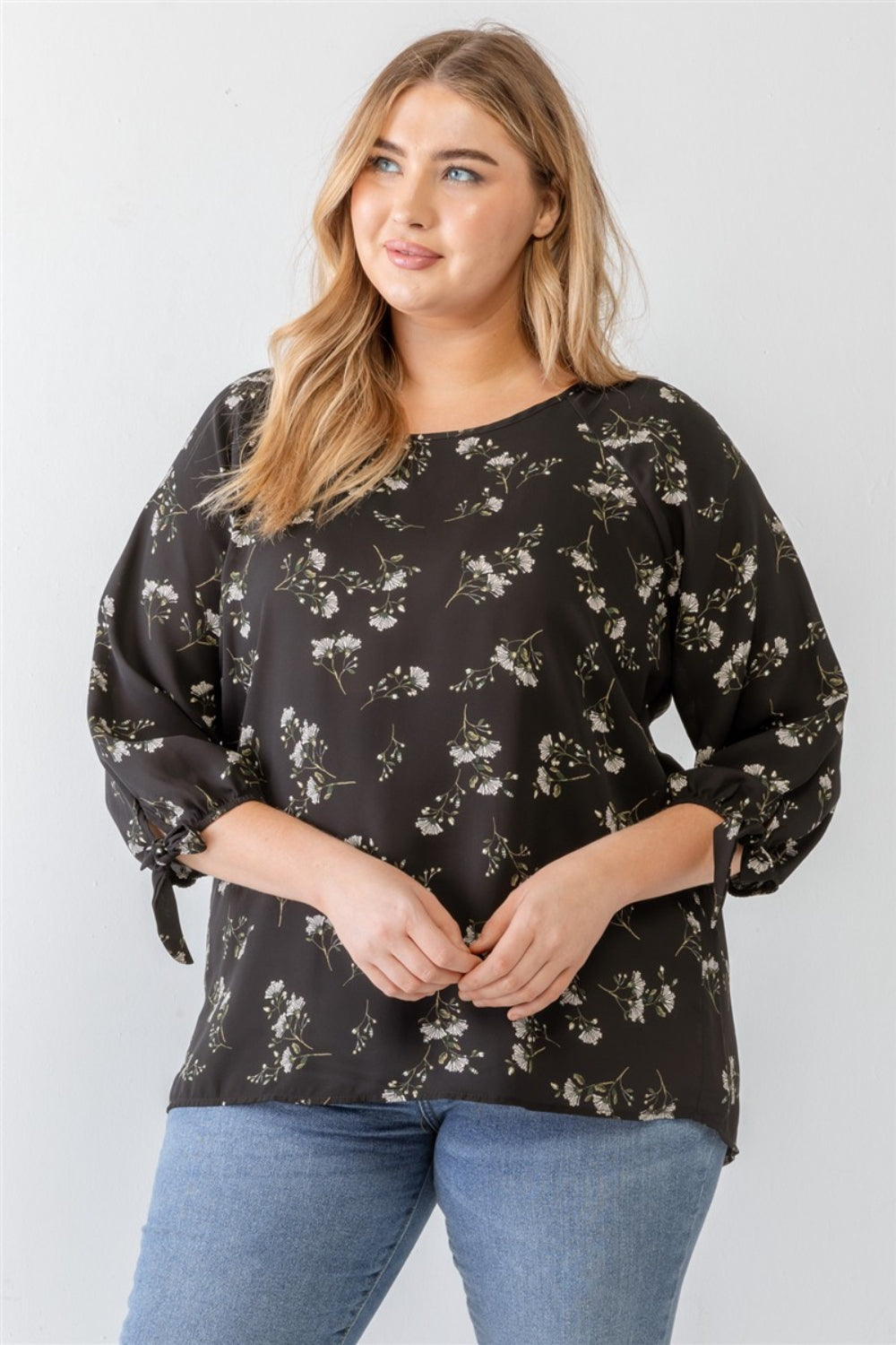 A person wearing a Zenobia Plus Size Floral Round Neck Blouse and blue jeans stands against a plain background.