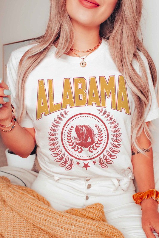 Person wearing an Alabama Graphic Tee made from 100% cotton, featuring a bear emblem, holding a drink in one hand.