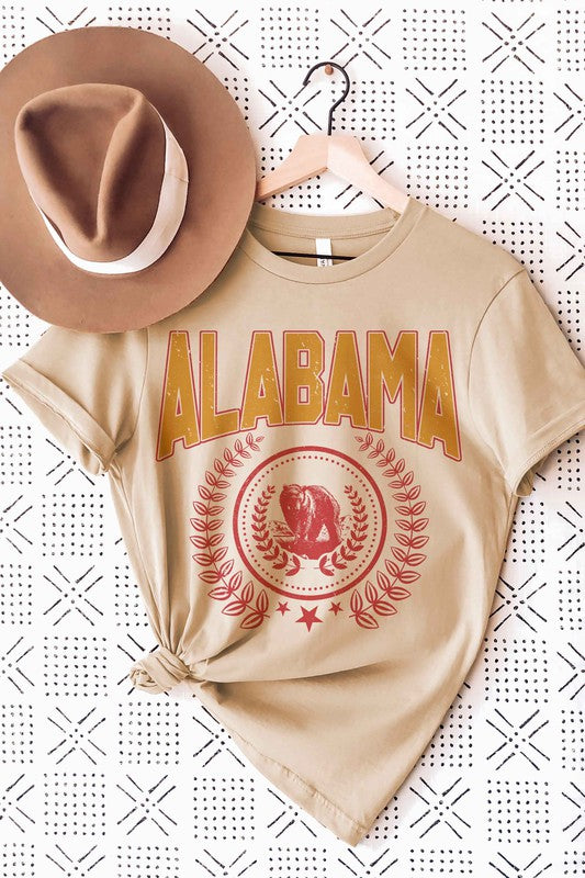 Person wearing an Alabama Graphic Tee made from 100% cotton, featuring a bear emblem, holding a drink in one hand.