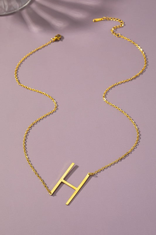 The Large Stainless Steel Initial Pendant Necklace features gold necklaces with prominent, capital letters "A," "B," and "C" set against a vibrant purple background, forming a stunning collection of initial pendants. Crafted from high-quality stainless steel, these pieces offer both durability and style.