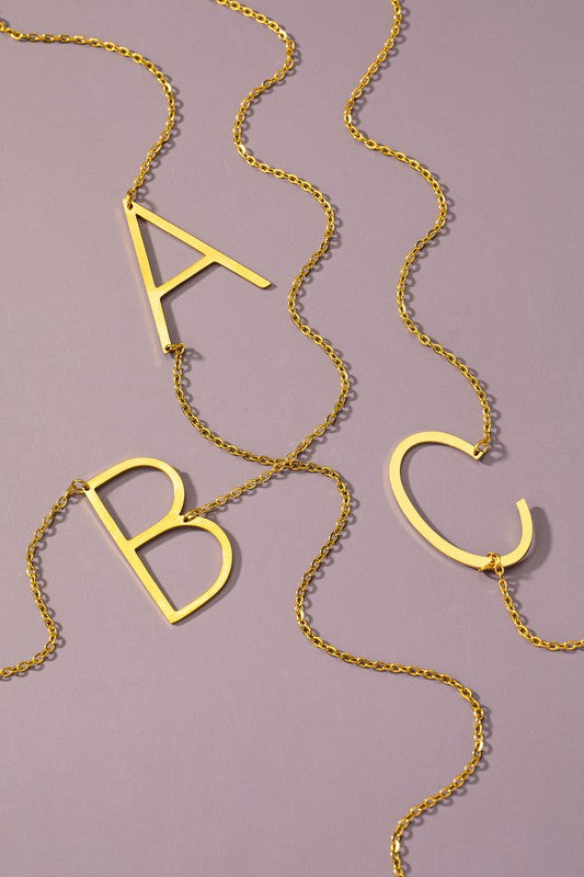 The Large Stainless Steel Initial Pendant Necklace features gold necklaces with prominent, capital letters "A," "B," and "C" set against a vibrant purple background, forming a stunning collection of initial pendants. Crafted from high-quality stainless steel, these pieces offer both durability and style.