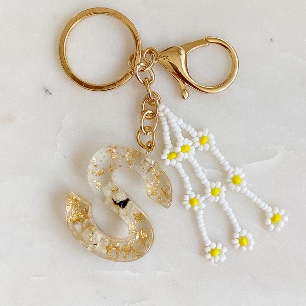 Baby Daisy Initial Key Chain alphabet keychains with real daisy flowers and gold flakes on a marble surface.
