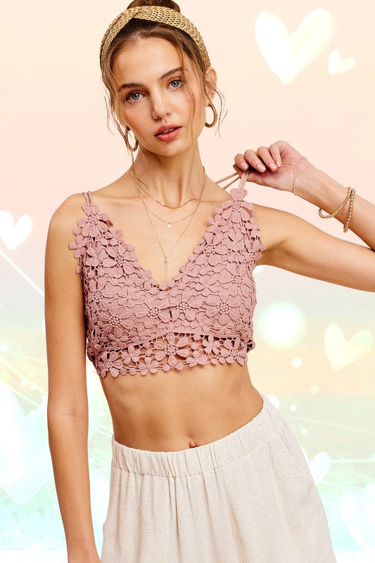 A woman poses wearing a white Crochet Lace Bralette Top with adjustable crisscross straps and reddish-orange pants with a smocked waist. A sun illustration is in the upper left corner of the image.