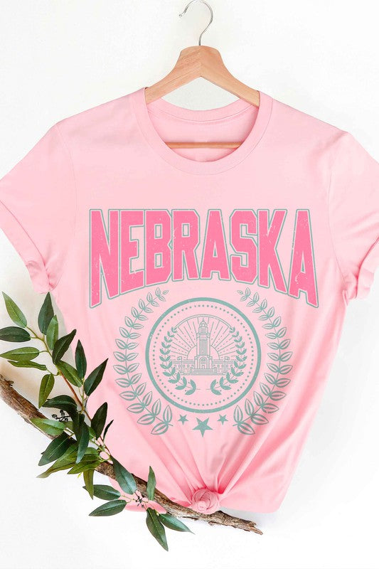 Person wearing the NEBRASKA GRAPHIC TEE in white, which features "Nebraska" in pink letters and a design beneath it, paired with white shorts. Made from 100% cotton, this tee ensures comfort and quality, making it perfect for plus-size fashion enthusiasts.