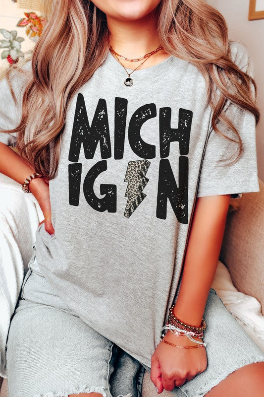 Someone sporting a MICHIGAN LEOPARD LIGHTNING GRAPHIC TEE and holding a drink, with the "I" in Michigan uniquely designed as a lightning bolt.