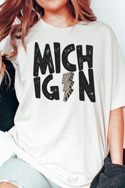 Someone sporting a MICHIGAN LEOPARD LIGHTNING GRAPHIC TEE and holding a drink, with the "I" in Michigan uniquely designed as a lightning bolt.