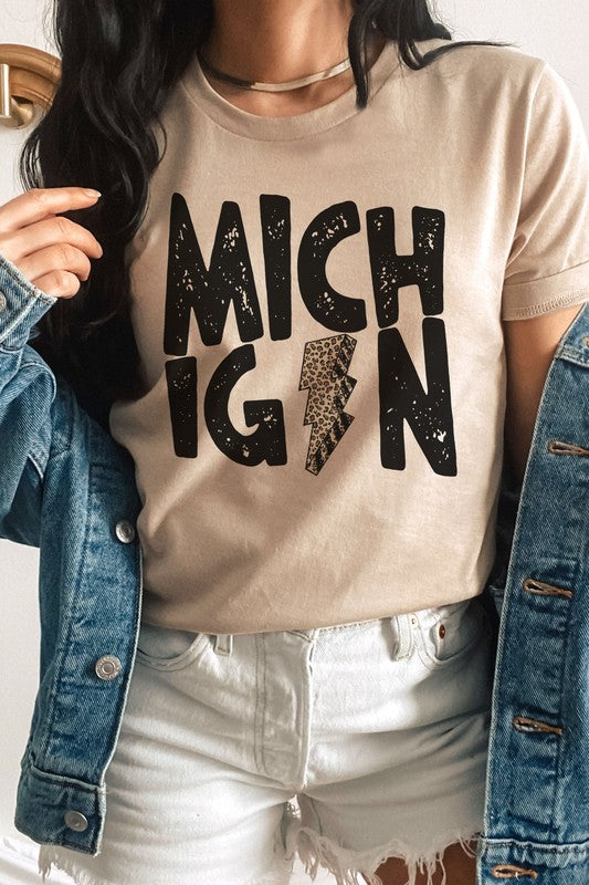 Someone sporting a MICHIGAN LEOPARD LIGHTNING GRAPHIC TEE and holding a drink, with the "I" in Michigan uniquely designed as a lightning bolt.