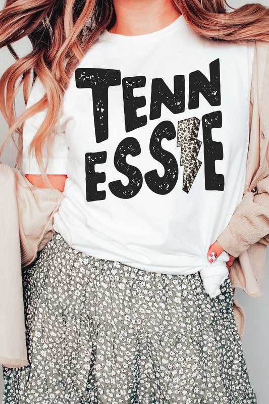 Wearing a gray TENNESSEE Leopard Lightning Graphic Tee with the word "TENNESSEE" prominently displayed in bold black letters and a lightning bolt design within the letter "E," this stylish unisex t-shirt provides an inclusive fashion choice for everyone.