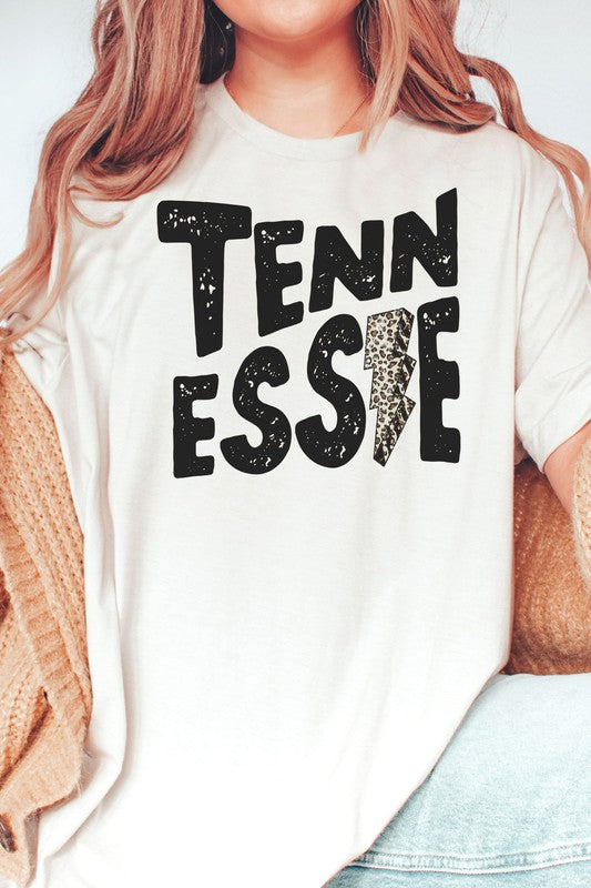 Wearing a gray TENNESSEE Leopard Lightning Graphic Tee with the word "TENNESSEE" prominently displayed in bold black letters and a lightning bolt design within the letter "E," this stylish unisex t-shirt provides an inclusive fashion choice for everyone.