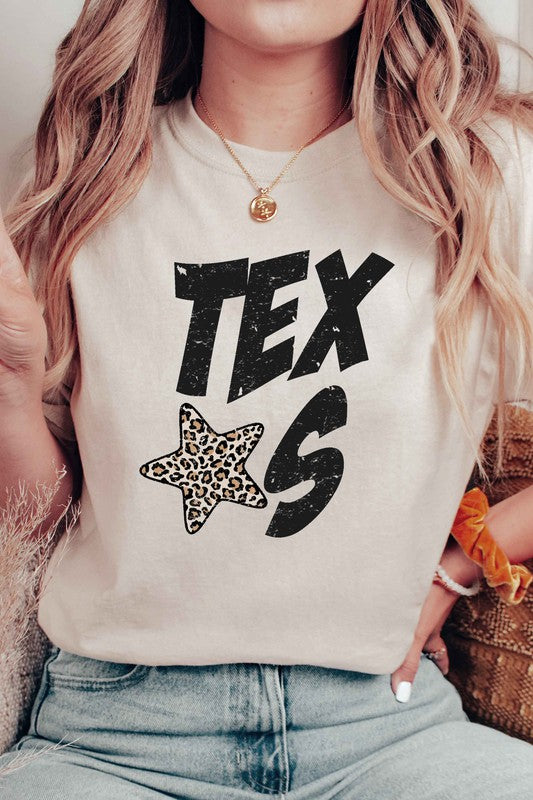 Person wearing a beige TEXAS LEOPARD STAR GRAPHIC TEE with black "TEXAS" text and a Texas leopard star. They also have long hair and a gold necklace. Unisex sizing available.