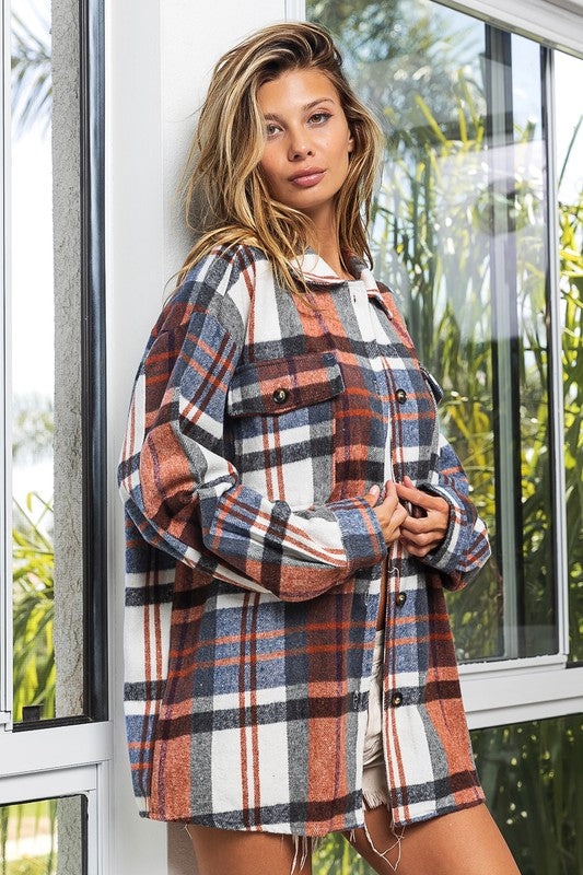 A woman in a Textured Shirt With Big Checkered Point leans casually against a wall, smiling while looking to the side. There are plants and a window in the background.