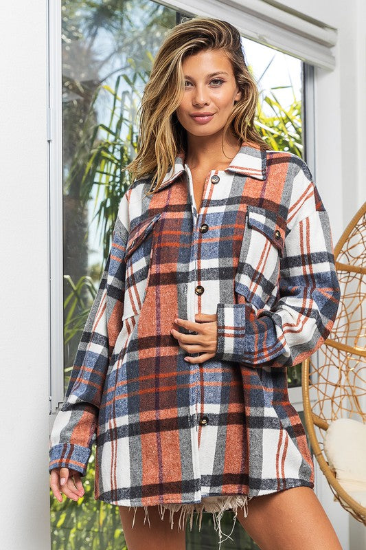 A woman in a Textured Shirt With Big Checkered Point leans casually against a wall, smiling while looking to the side. There are plants and a window in the background.