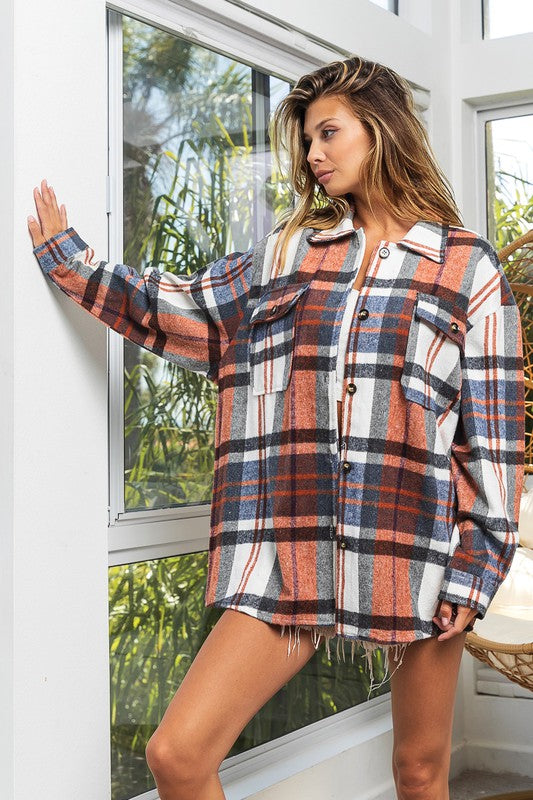 A woman in a Textured Shirt With Big Checkered Point leans casually against a wall, smiling while looking to the side. There are plants and a window in the background.