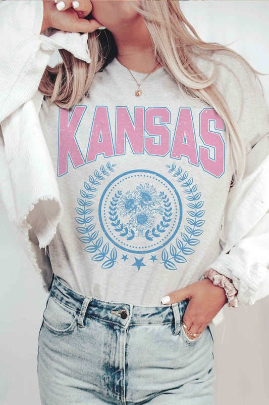 Person wearing the KANSAS GRAPHIC TEE, featuring "KANSAS" printed in pink letters above a blue floral and laurel wreath design. Unisex sizing is available, ensuring a perfect fit for everyone.