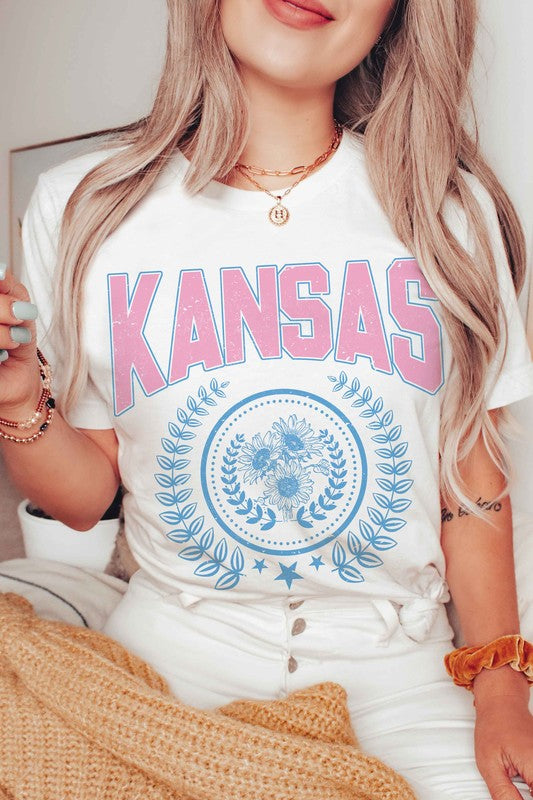 Person wearing the KANSAS GRAPHIC TEE, featuring "KANSAS" printed in pink letters above a blue floral and laurel wreath design. Unisex sizing is available, ensuring a perfect fit for everyone.