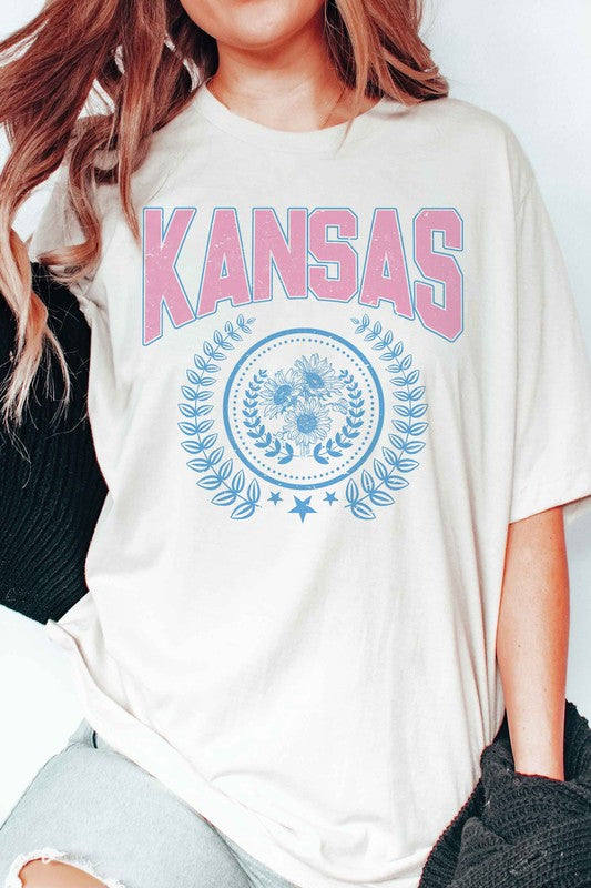 Person wearing the KANSAS GRAPHIC TEE, featuring "KANSAS" printed in pink letters above a blue floral and laurel wreath design. Unisex sizing is available, ensuring a perfect fit for everyone.