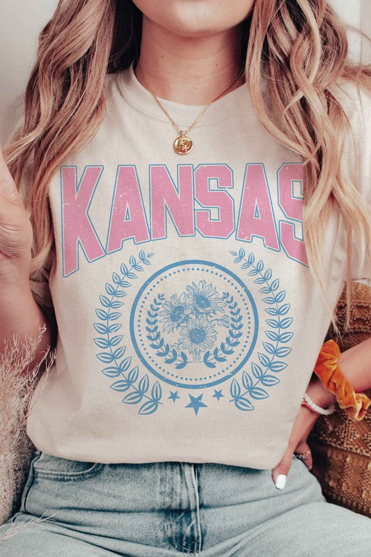 Person wearing the KANSAS GRAPHIC TEE, featuring "KANSAS" printed in pink letters above a blue floral and laurel wreath design. Unisex sizing is available, ensuring a perfect fit for everyone.