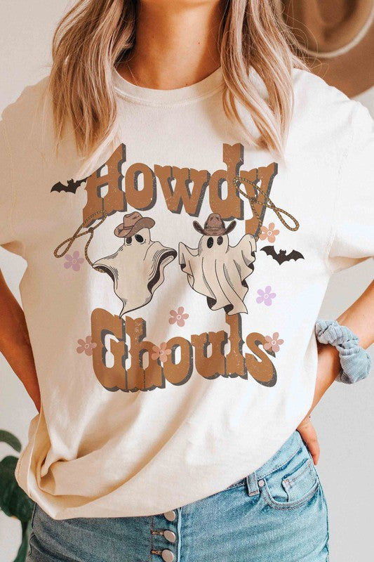 Person wearing the HOWDY GHOULS GRAPHIC TEE, a white unisex shirt featuring the text "Howdy Ghouls" and illustrations of two ghosts in cowboy hats, designed for a perfect fit.