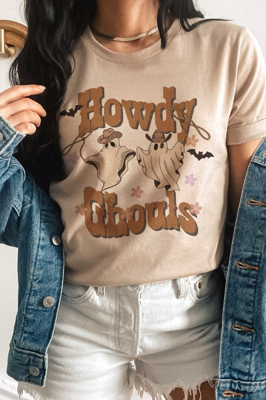 Person wearing the HOWDY GHOULS GRAPHIC TEE, a white unisex shirt featuring the text "Howdy Ghouls" and illustrations of two ghosts in cowboy hats, designed for a perfect fit.