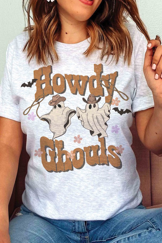 Person wearing the HOWDY GHOULS GRAPHIC TEE, a white unisex shirt featuring the text "Howdy Ghouls" and illustrations of two ghosts in cowboy hats, designed for a perfect fit.