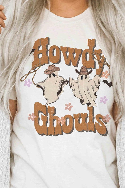 Person wearing the HOWDY GHOULS GRAPHIC TEE, a white unisex shirt featuring the text "Howdy Ghouls" and illustrations of two ghosts in cowboy hats, designed for a perfect fit.