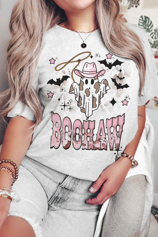 A person wearing a unisex BOOHAW COWBOY GHOST GRAPHIC TEE, made of 100% cotton, featuring a graphic of a Cowboy Ghost in a white T-shirt and the word "BOOHAW" in pink western-style lettering.